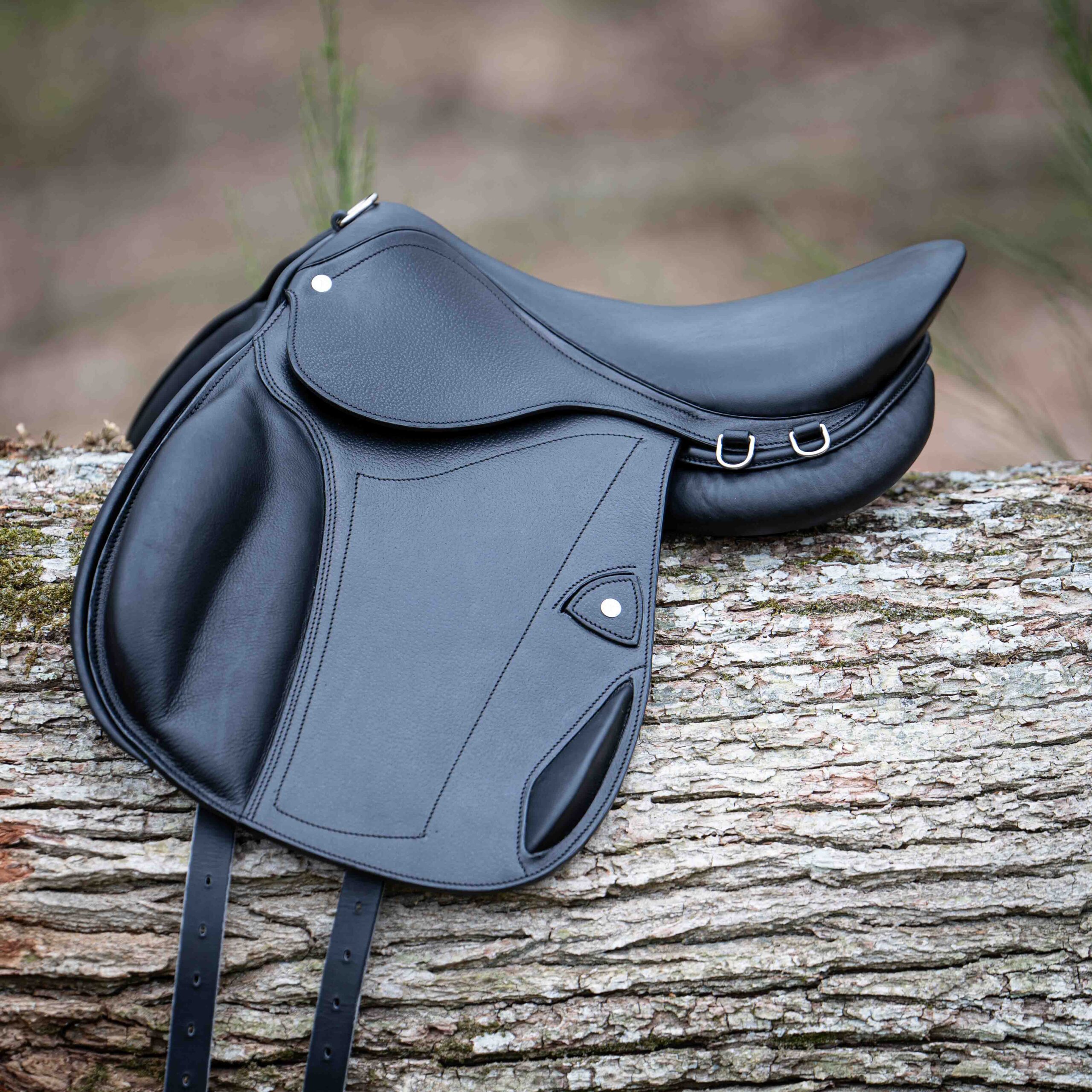 Selle d'équitation en cuir noir modèle Bocage, quartiers longs et taquets, posée en extérieur