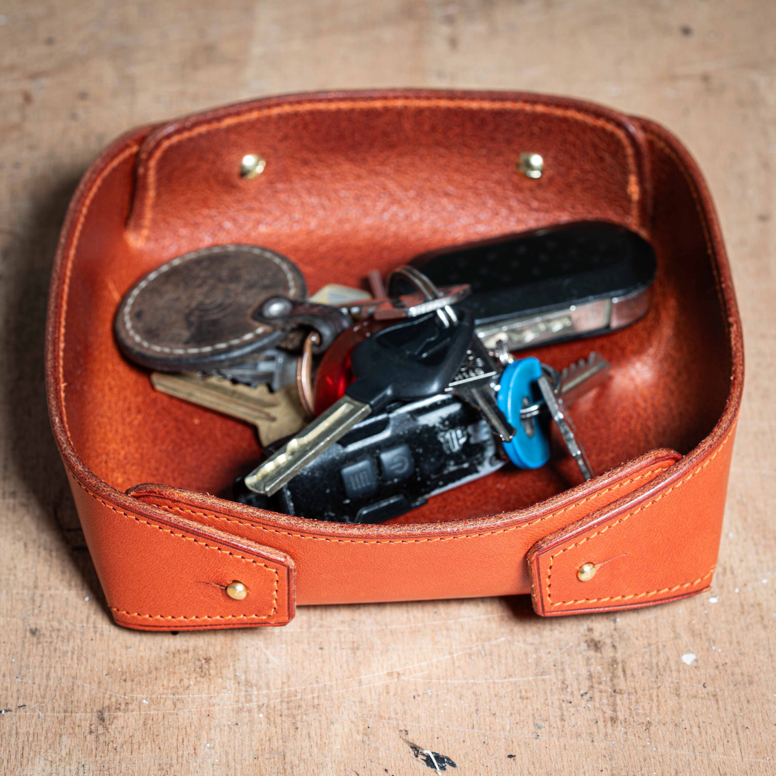 Vide-poche-cuir-sellerie-valle-orange-vitrine Gros plan d'une ceinture artisanale en cuir pleine fleur cognac avec boucle en laiton massif. C'est simple, descriptif et efficace.